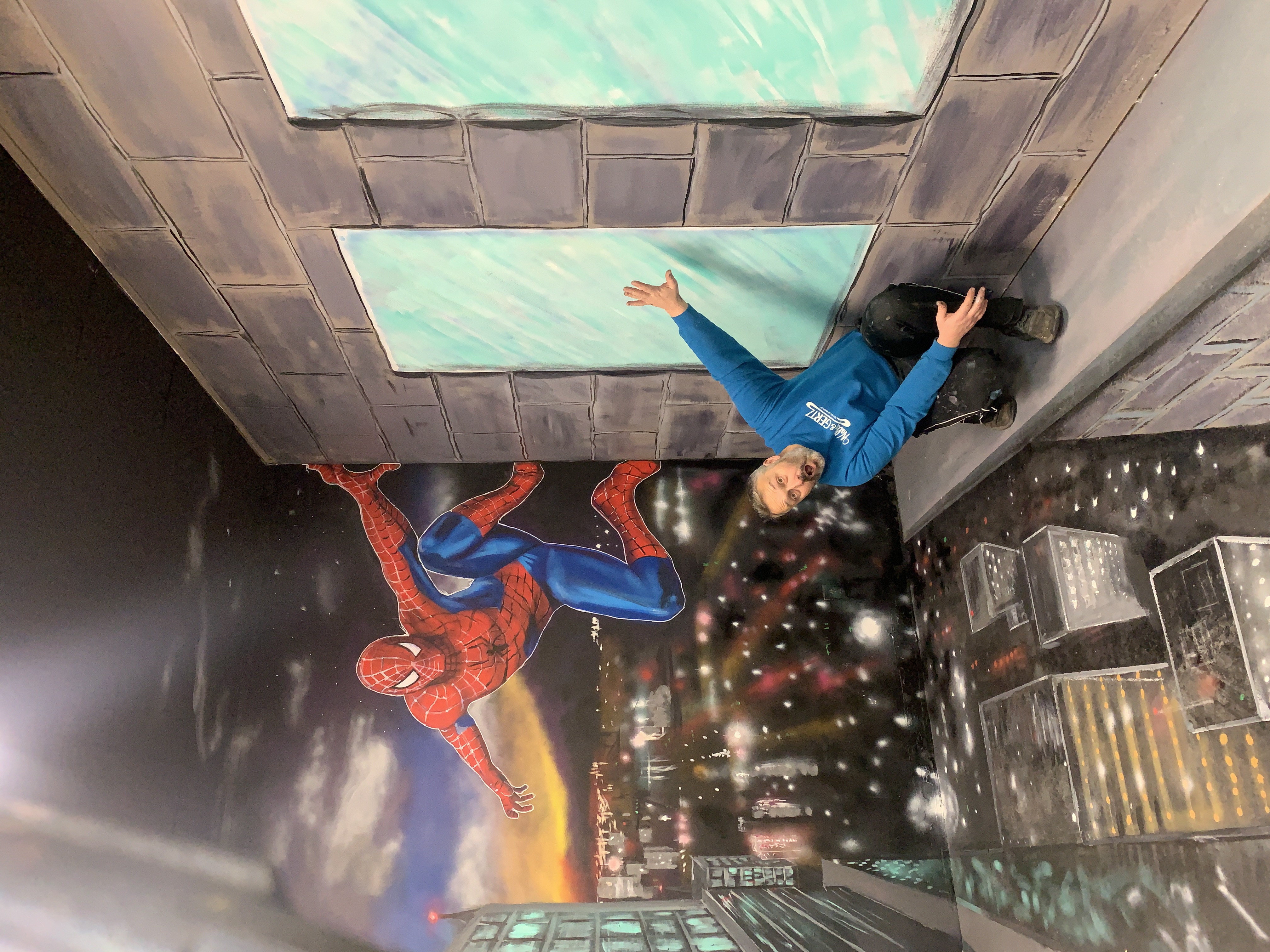 Spectacular 3D illusion Spiderman climbing a building wall with city skyline visible below