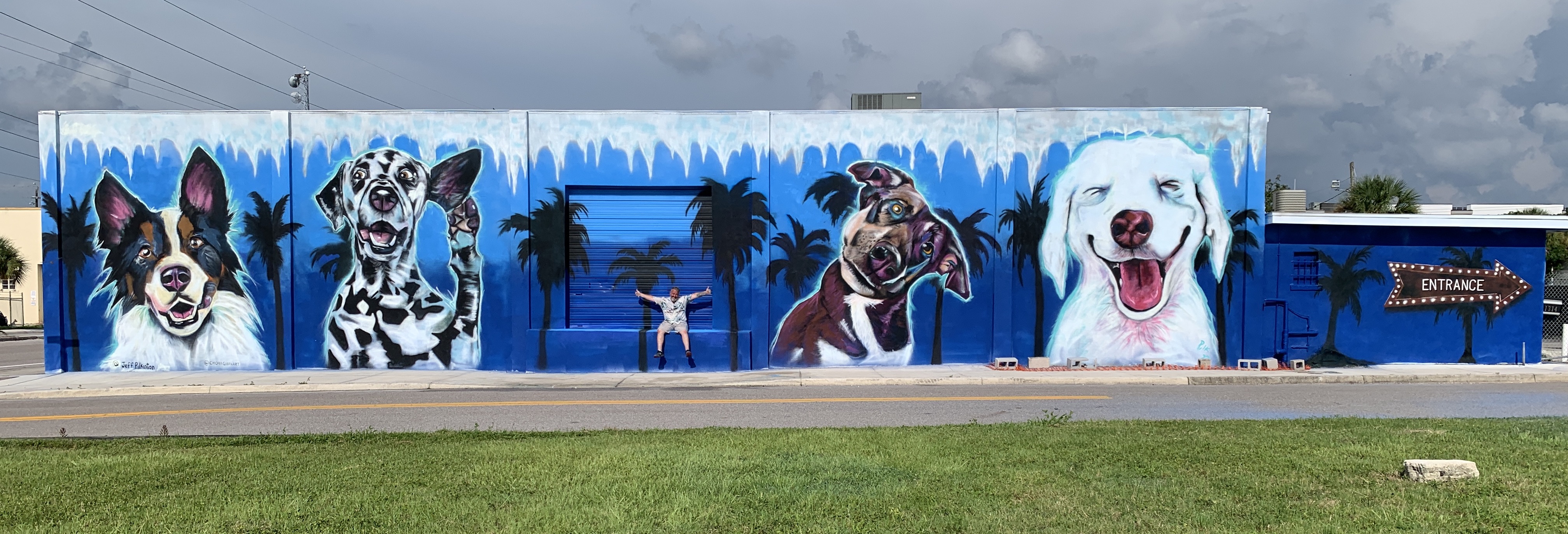 Playful mural of happy dogs with tropical palm trees and entrance on blue commercial building exterior